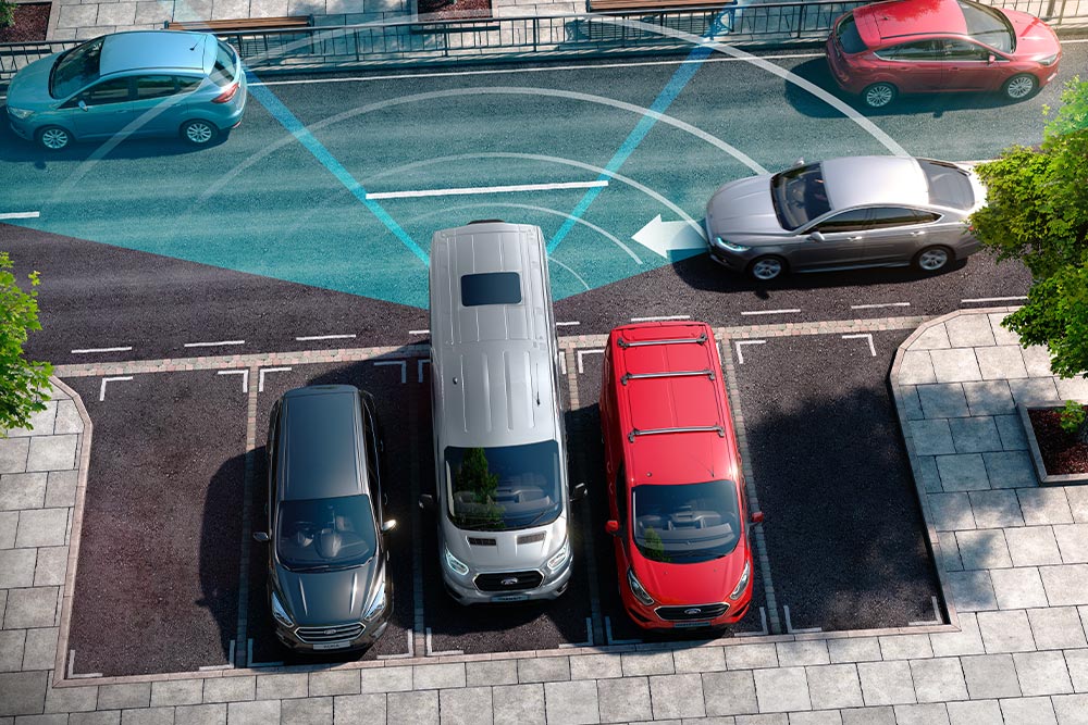 Carrinha Ford Transit prateada a fazer marcha-atrás, com linhas azuis a indicar a utilização do sensor de estacionamento traseiro.