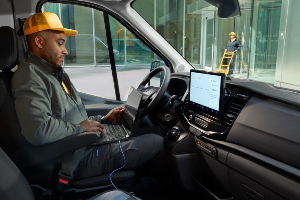 Homem sentado no lugar do condutor de uma carrinha Ford Transit, a usar um portátil.