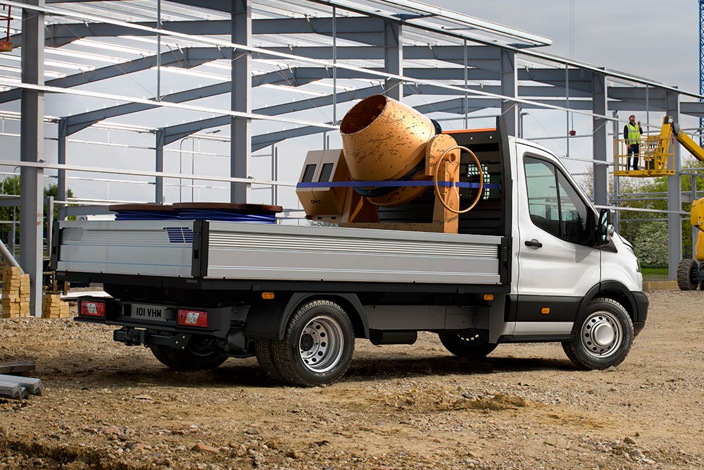 Ford Transit Chassis Cabina a transportar uma betoneira na caixa de carga, estacionada num estaleiro de obras. 