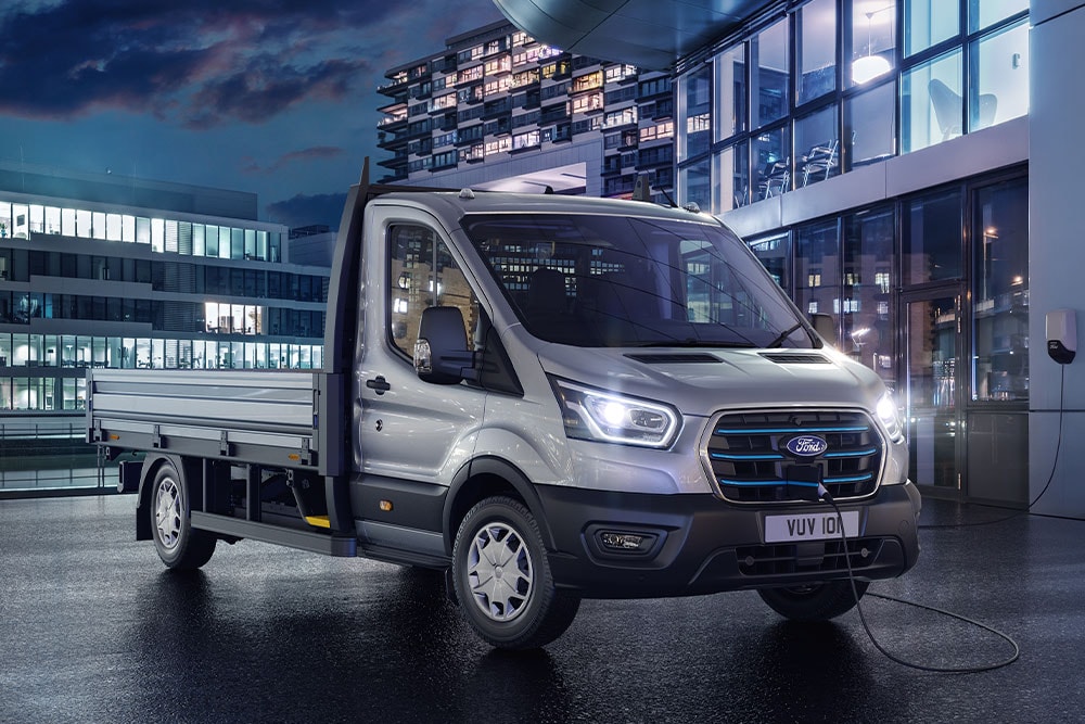 Ford E-Transit Chassis Cabina prateada estacionada em frente a um edifício moderno, de noite.
