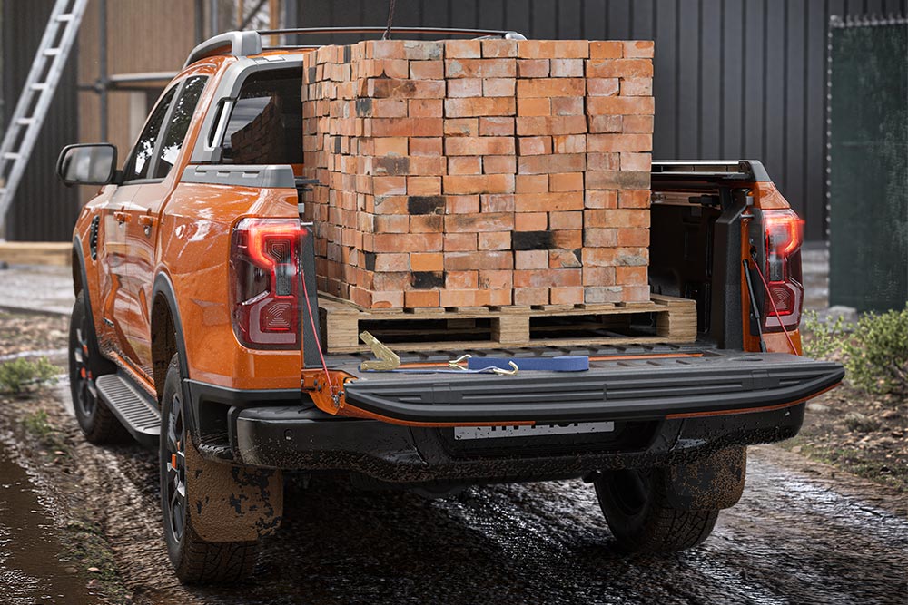 Vista da parte de trás de uma Ford Ranger laranja, uma pilha de tijolos carregados na plataforma.