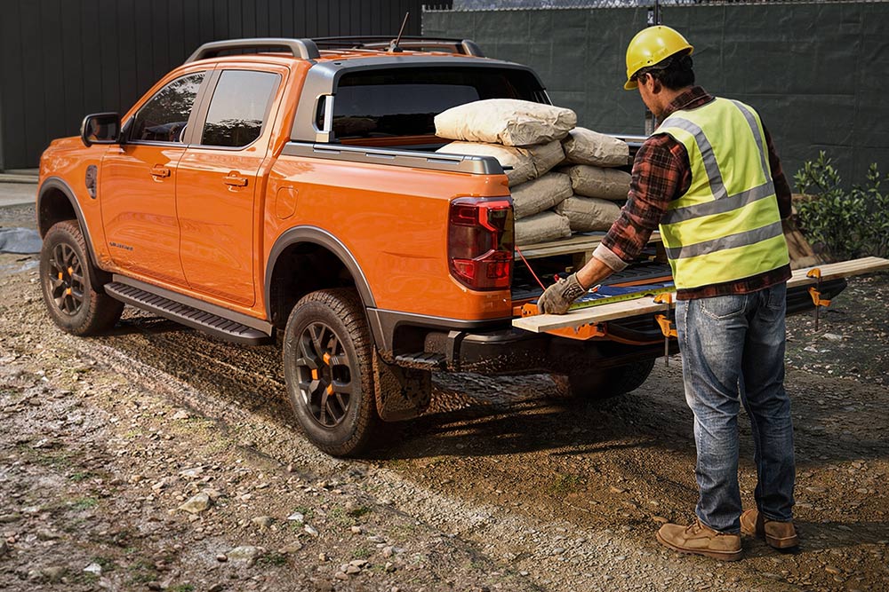 Um operário da construção civil a transportar equipamento na caixa de uma Ford Ranger laranja.