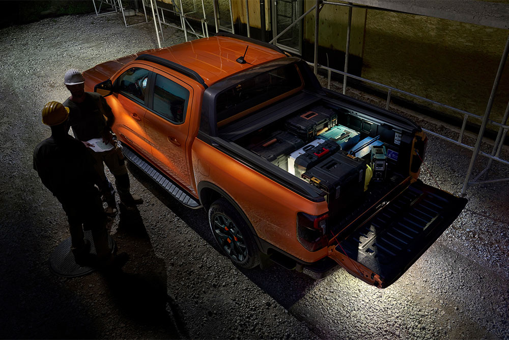 Vista aérea noturna da Ford Ranger Wildtrak laranja, a mostrar a iluminação da zona exterior.