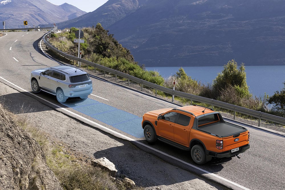 Uma Ford Ranger laranja utiliza o seu sistema avançado de assistência ao condutor ao longo de uma autoestrada costeira.