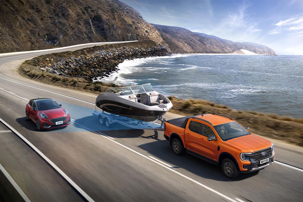 Uma Ford Ranger laranja reboca um barco ao longo de uma autoestrada costeira, demonstrando a sua capacidade de reboque.