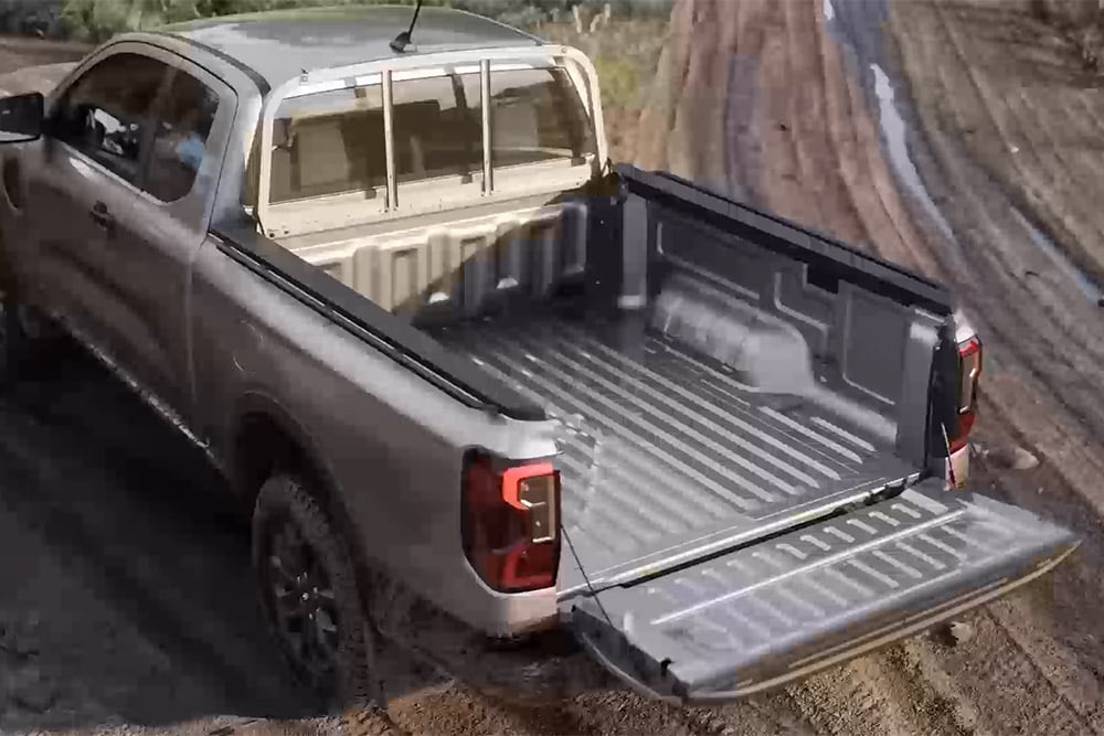 Uma Ford Ranger XLT Super Cab prateada, estacionada numa superfície enlameada com a porta da bagageira aberta, vista de cima.