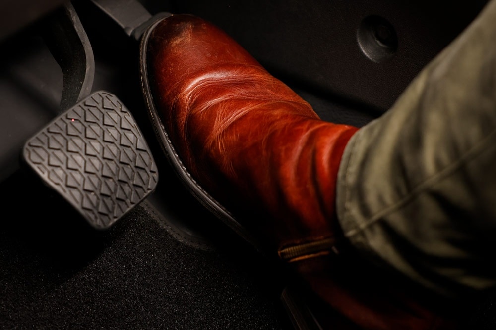 O pé de uma pessoa com uma bota castanha repousa no pedal do acelerador de um veículo