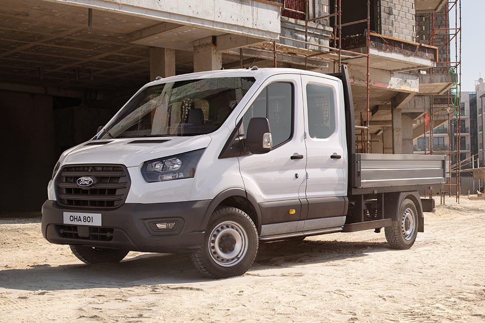 Um Ford Transit Custom branco com chassis-cabina e plataforma está estacionado num local de construção.