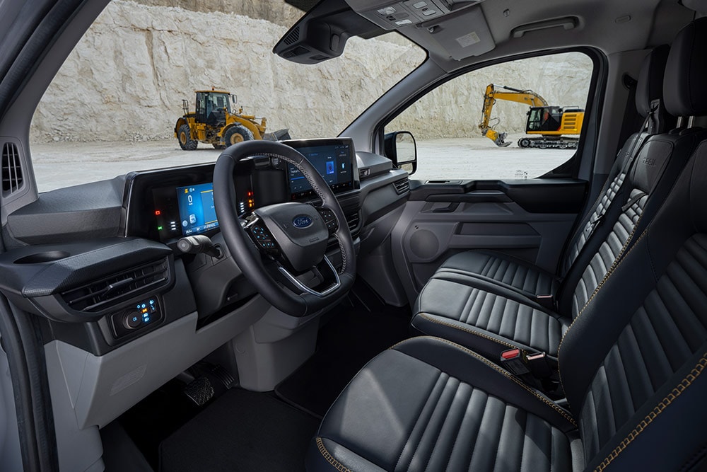 Vista interior de uma carrinha Ford Transit Custom, a mostrar o painel, o volante e os bancos.