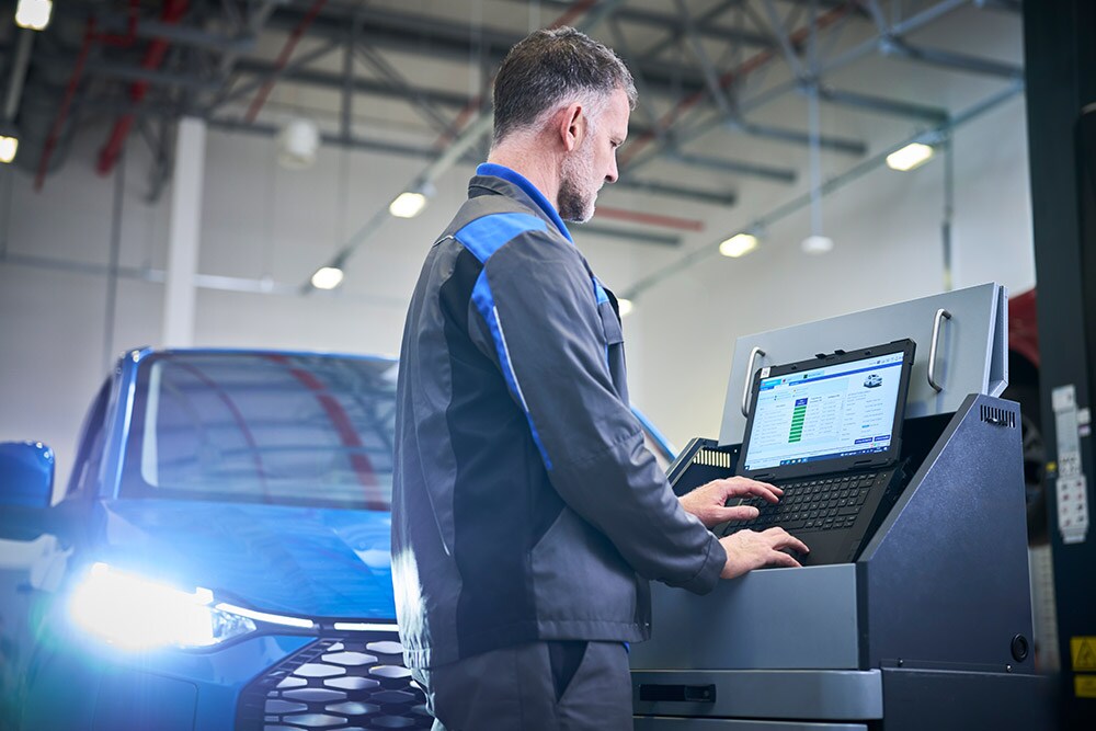 Um técnico a trabalhar num portátil ligado a um SUV Ford azul numa área de serviço.