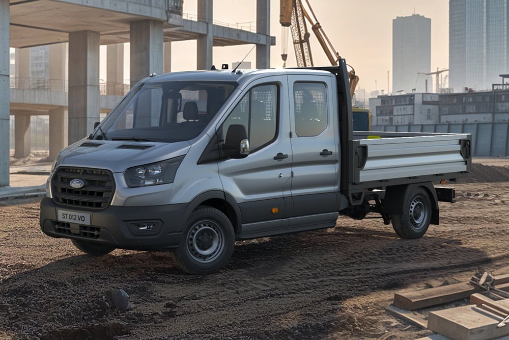 Um Ford Transit basculante cinzento numa obra urbana, com edifícios em construção e uma grua ao fundo.