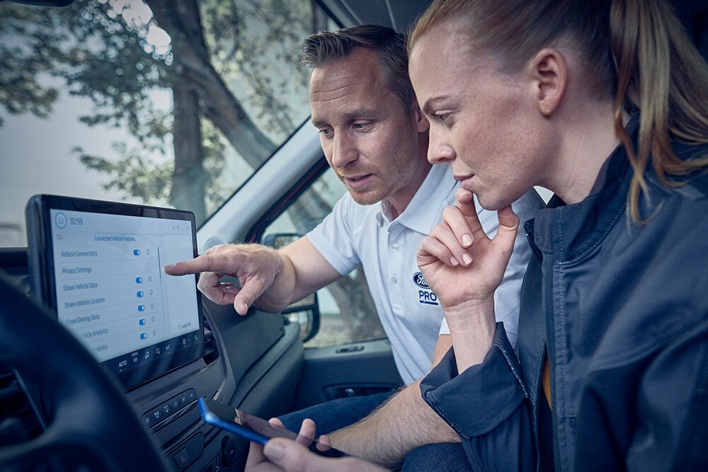 A Ford Pro uptime expert discussing fleet data with a customer, displayed on the digital screen of a Ford Transit van.