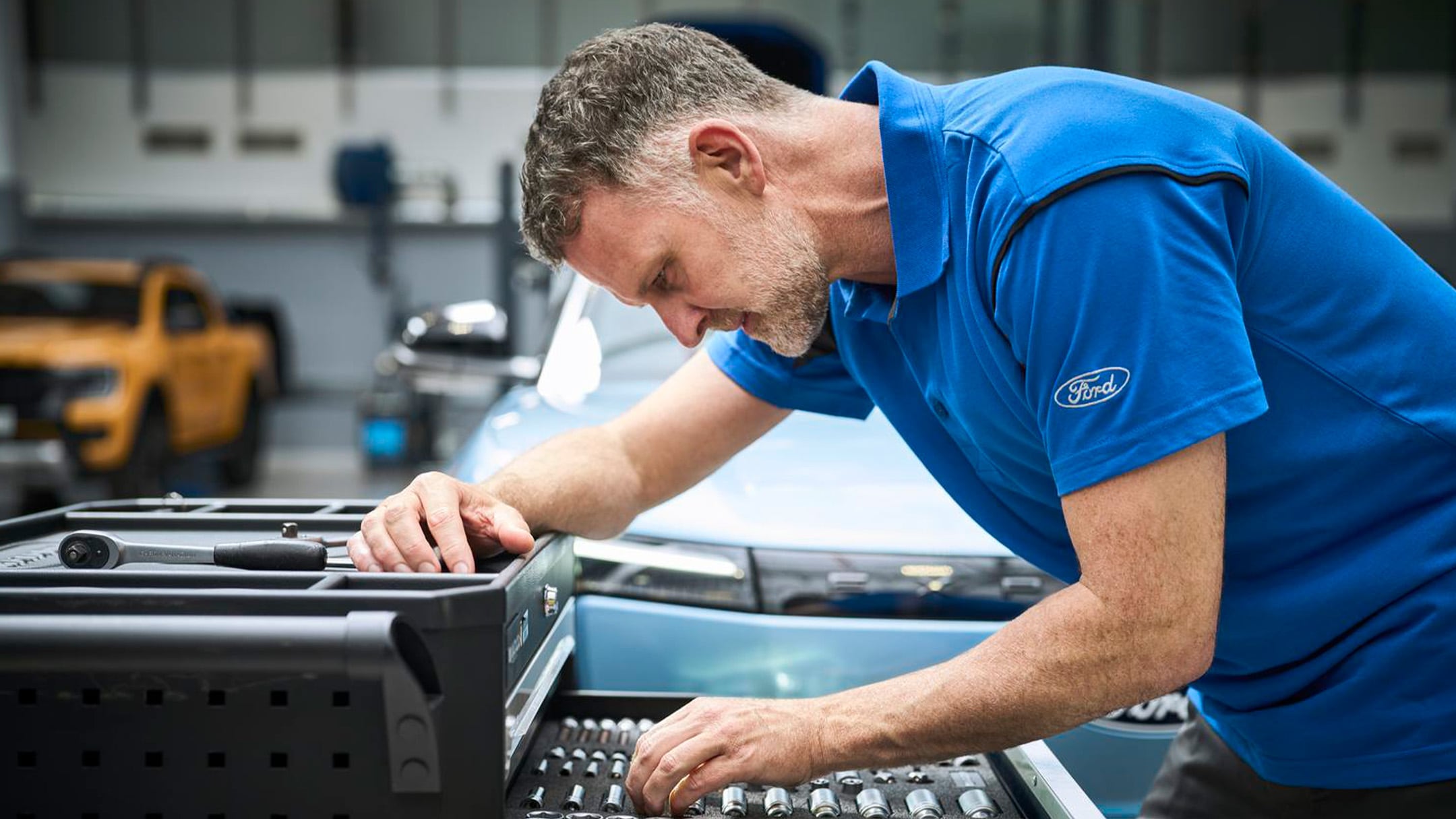 Um especialista da Ford Pro, sentado num carro, verifica um portátil durante uma revisão de um veículo Ford.