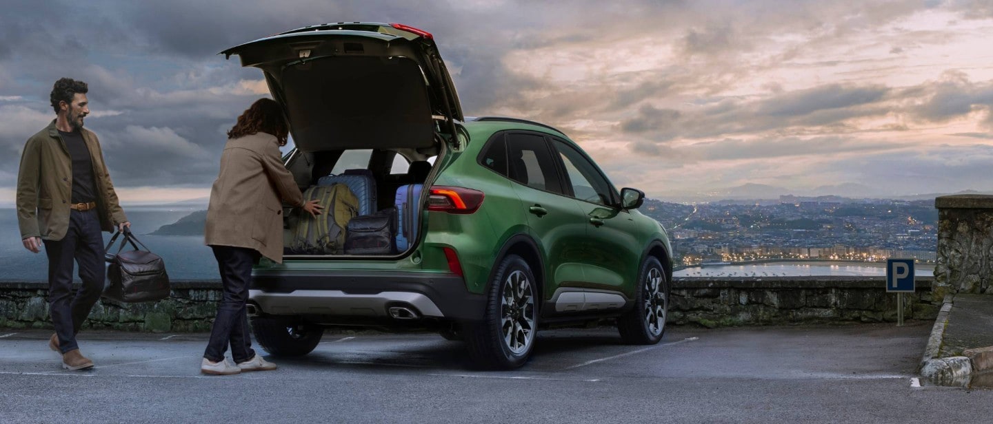 Um homem e uma mulher a colocar bagagem na bagageira de um SUV verde estacionado Um homem e uma mulher a colocar bagagem na bagageira de um SUV verde estacionado